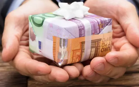 Dłonie trzymają prezent opakowany w banknoty euro. To pomysł, jak zapakować pieniądze na prezent dla dziecka, tworząc unikalną niespodziankę.