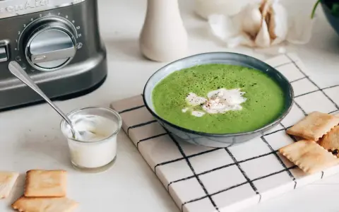 Une délicieuse soupe de légumes variés, onctueuse et verte, garnie de crème et servie avec des crackers.
