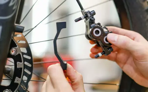 Hände montieren eine Fahrrad-Scheibenbremse. Ein Adapter wird gehalten, um ein Schleifen der Scheibenbremse zu verhindern.