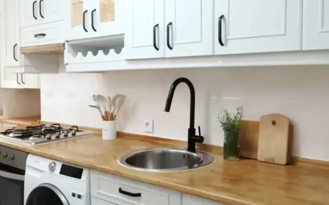 Cocina renovada: gabinetes blancos, encimera de madera y grifo negro. ¡Un ejemplo de cómo pintar muebles de melamina para darles nueva vida!
