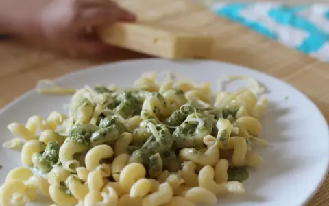 Pyszny makaron ze szpinakiem i parmezanem, gotowy do podania. Dziecko pomaga w przygotowaniu.