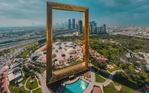 Dubai Frame rahmt die Skyline und die futuristischen Dubai Projekte ein. Ein Park mit Kuppeln und ein Pool sind im Vordergrund.