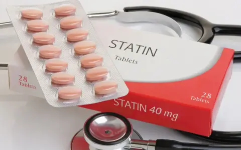 Opakowanie tabletek statynowych i blister z tabletkami. Stetoskop w tle. Statyny na co? Na obniżenie cholesterolu.