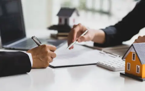 Signature d'un accord pour la résiliation d'un mandat exclusif après 3 mois. Des maisons miniatures et un ordinateur sont visibles.