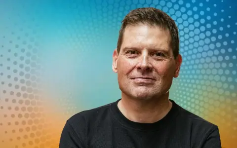 Porträt eines Mannes mit freundlichem Lächeln vor einem bunten Hintergrund. Man fragt sich, was macht Jan Ullrich heute?
