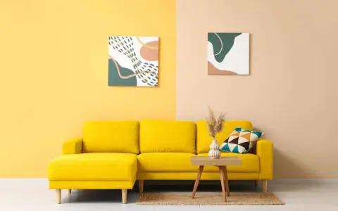 Un divano giallo acceso in una stanza con pareti bicolore. I colori della stanza sono vivaci e moderni, con due quadri astratti che completano l'arredamento.