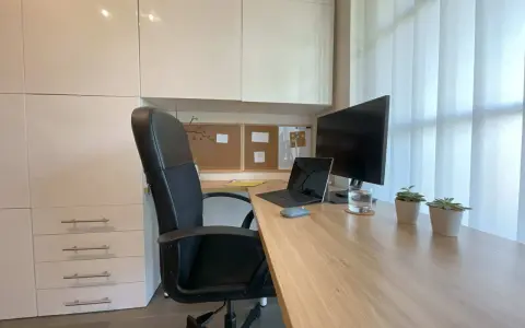 Un coin bureau moderne et fonctionnel pour aménager votre espace de travail. Chaise noire, bureau en bois, écran, ordinateur portable et plantes vertes.