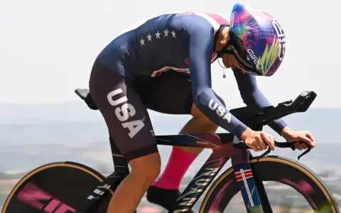 Chloé Dygert, in her USA cycling kit, races against the clock, her focus intense as she powers her bike uphill.