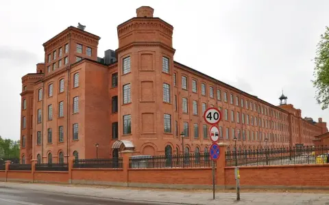 Imponujący ceglany budynek dawnego Księży Młyn, idealny na zwiedzanie. Widać znaki drogowe i ogrodzenie.