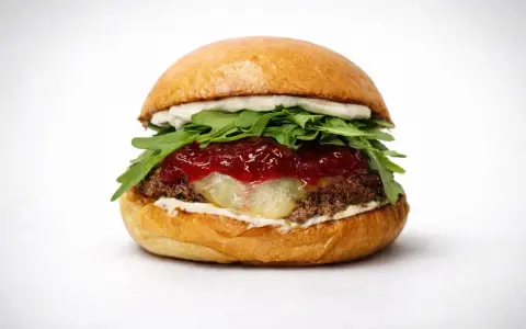 Soczysty burger z rukolą, konfiturą i roztopionym serem na białym tle.