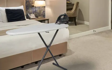 Deska do prasowania z żelazkiem na łóżku w hotelowym pokoju.