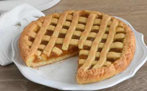 Crostata con marmellata, un classico della crostata ricetta tradizionale, servita su un piatto bianco con un tovagliolo di lino.