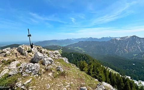 Gipfelkreuz am Fockenstein bei Lenggries, mit Blick über Wälder und Berge bis zum See.
