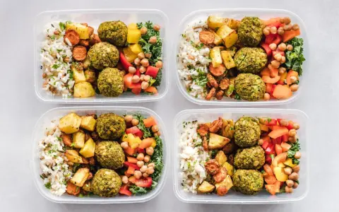 Vier Behälter mit gesunden meal prep Rezepten: Reis, Falafel, geröstetes Gemüse und Salat.