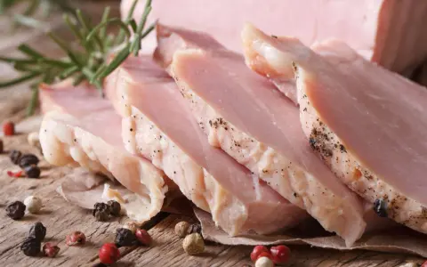 Super delikatny i soczysty schab gotowany, pokrojony w plastry, z gałązką rozmarynu i ziarnami pieprzu.