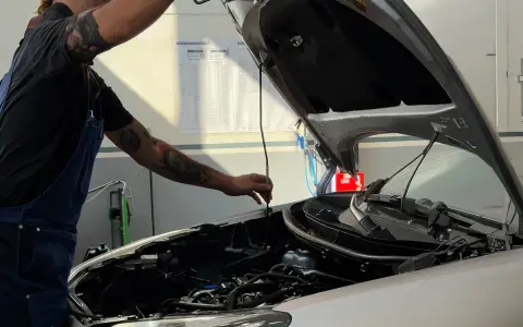 Meccanico con tatuaggi controlla il motore. Capire la differenza tra tagliando e revisione è fondamentale per la manutenzione dell'auto.