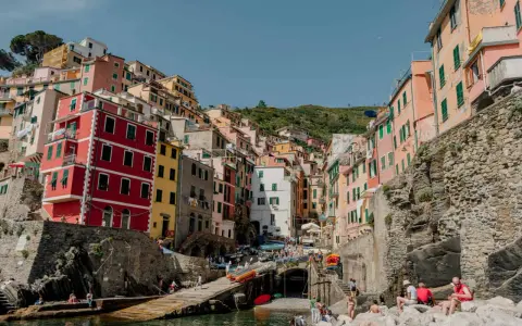 Colorful buildings cling to a hillside overlooking a harbor, a picturesque scene after a train from Bologna to Cinque Terre.