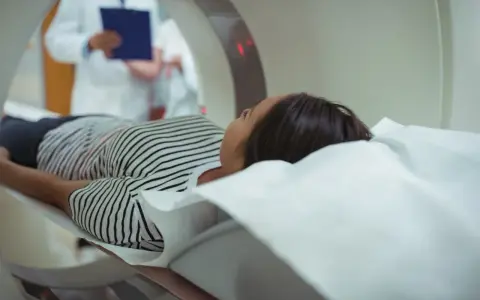 Pacjentka leży na łóżku rezonansu magnetycznego, obok niej stoi lekarz z dokumentacją.