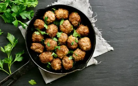 Polpette al forno dorate e succulente, guarnite con prezzemolo fresco, in una padella di ghisa su sfondo scuro.