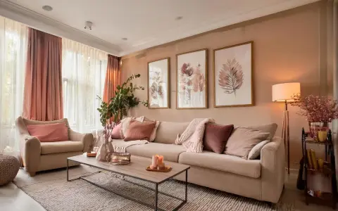 Un salon coloré et chaleureux, avec un canapé beige, des coussins roses et des tableaux de feuilles.