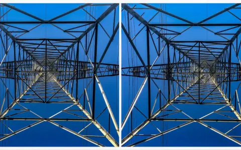 Widok z dołu na kratownicę słupa energetycznego, tworzącą geometryczny wzór na tle błękitnego nieba. To fotografia stereoskopowa.
