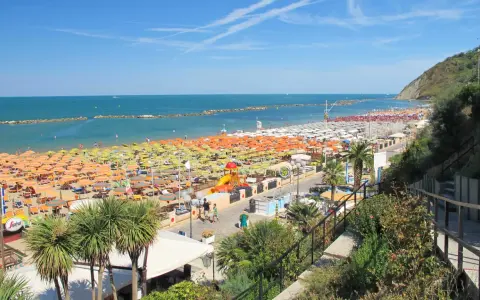 Spiaggia affollata a Gabicce Mare, con file infinite di ombrelloni colorati e lettini. Le recensioni la descrivono come un paradiso estivo.