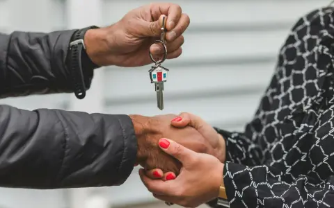 Une main tend une clé de maison, l'autre la saisit. Une poignée de main scelle un accord, peut-être une solution quand un indivisaire ne paye pas.