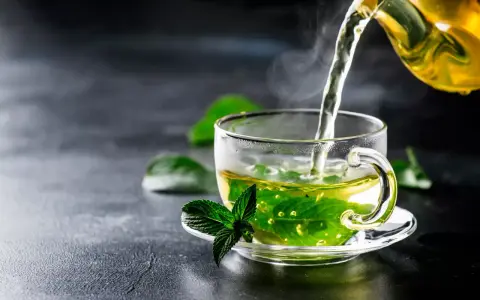 Un thé fumant à la menthe poivrée est versé dans une tasse transparente, ornée d'une feuille de menthe fraîche.