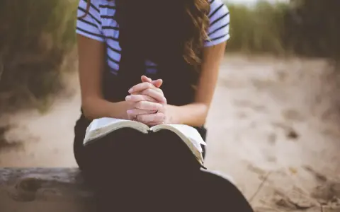 Kobieta z dłońmi złożonymi nad otwartą Biblią. To jej modlitwa o dobry dzień w pracy.