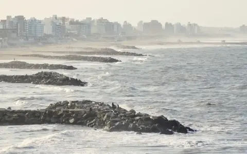 Olas rompen contra una escollera de rocas, protegiendo una ciudad costera. El escollera significado es claro: barrera contra el mar.