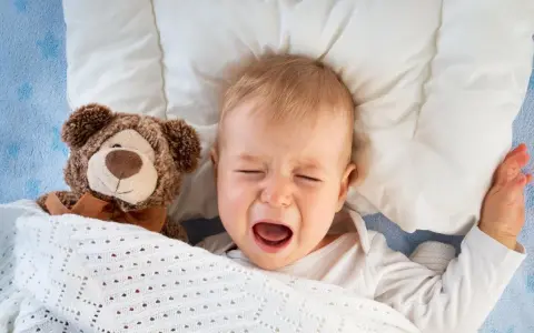 Bebé llorando en la cama con su osito de peluche. Mi hijo de 2 años se despierta mucho por la noche.
