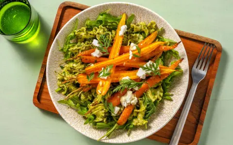 Pâtes vertes avec des carottes rôties et du fromage émietté, garnies de fanes de carottes fraîches.