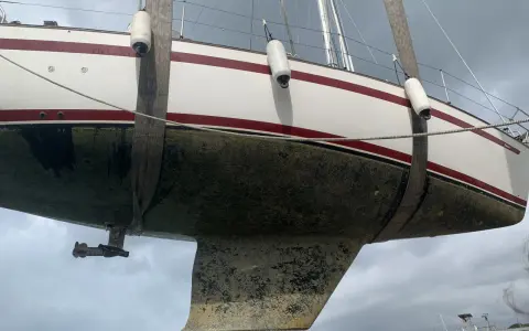 Segelboot wird angehoben, der Rumpf ist mit Algen bedeckt und bereit für die Behandlung mit Epoxidharz zum Streichen.