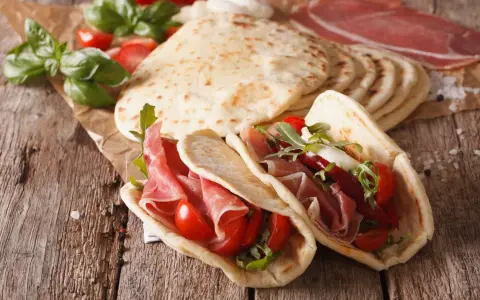 Piadina romagnola, un piatto tipico di Rimini, farcita con prosciutto crudo, pomodorini e rucola.