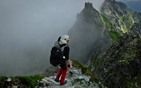 Osoba w kasku i z plecakiem przemierza skalisty szlak. Wspaniała przygoda w górach, prawdziwa turystyka piesza.