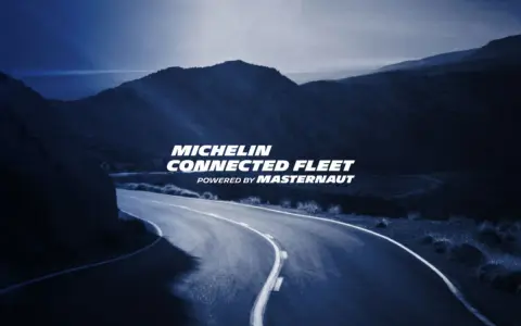 Carretera sinuosa bajo un cielo azul oscuro, con el texto "MICHELIN CONNECTED FLEET" iluminado.