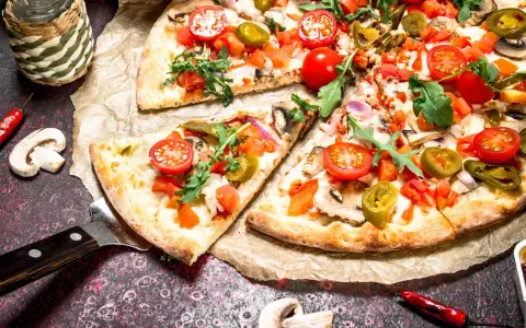 Kawałki pizzy z pomidorkami, jalapeno i rukolą na papierze do pieczenia.