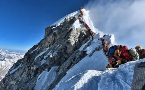 Kolejka ludzi wspinających się na najwyższą górę na świecie, Everest. Wspinacze w kolorowych kurtkach i z plecakami pokonują śnieżne zbocza.