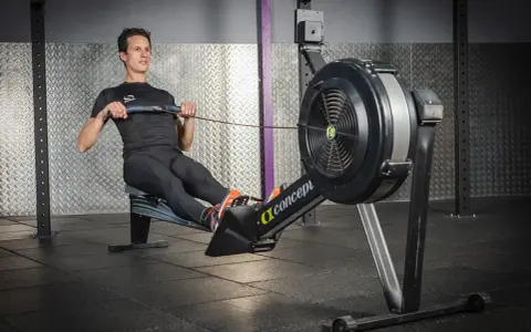 Un homme en tenue de sport effectue un exercice rameur dans une salle de sport.
