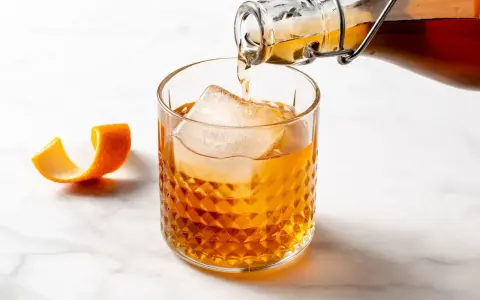 Amaretto co to? Bursztynowy likier z migdałów i moreli, nalewany do szklanki z lodem, z ozdobną skórką pomarańczy.