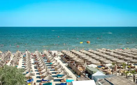 Słoneczna plaża w Rumunii, pełna leżaków i parasoli. Ludzie kąpią się w morzu, idealne miejsce na wakacje.