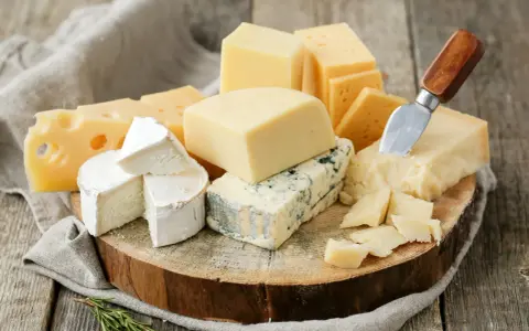 Różnorodne sery ostre gatunki: pleśniowy, żółty z dziurami, brie i parmezan, ułożone na drewnianej desce z gałązką rozmarynu.