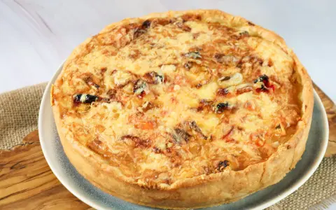 Eine goldbraune Sommer Quiche mit geschmolzenem Käse und bunten Gemüsestückchen, bereit zum Genießen.