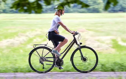 Kobieta w kasku jedzie na rowerze trekkingowym po ścieżce w parku.