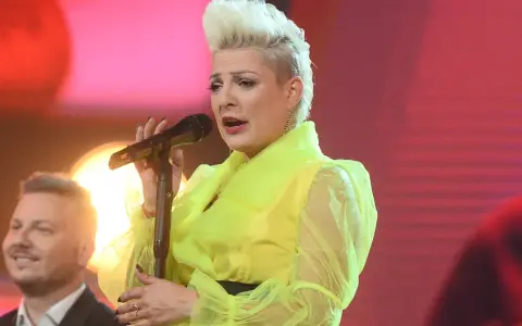 Wokalistka w neonowej kreacji śpiewa canzone d'amore, a obok niej mężczyzna z uśmiechem na twarzy.