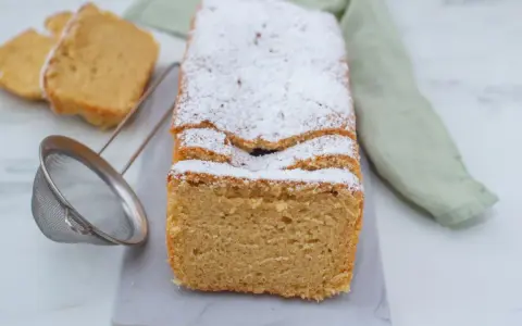 Puszyste keto ciasto z mikrofali, posypane cukrem pudrem, prezentuje się apetycznie. Obok leżą dwa kawałki ciasta i sitko.