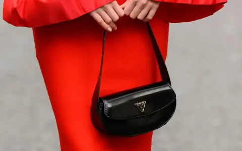 Elegancka, mała torebka Guess w kolorze czarnym, noszona do czerwonej sukienki.