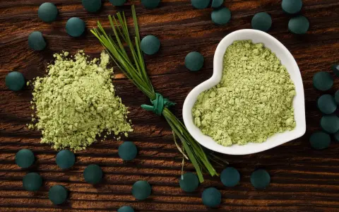 Zielony proszek i tabletki na drewnianym tle. Dowiedz się, spirulina co to za superfood!