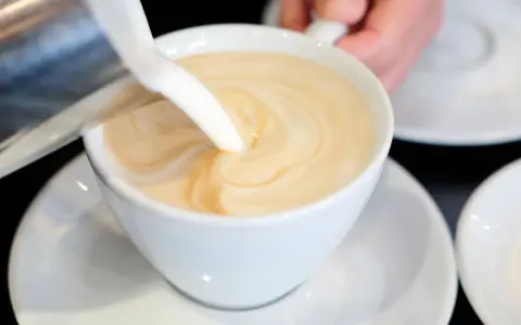 Milch wird in eine Tasse mit Kaffee gegossen, um ein cremiges Café au Lait zu kreieren.