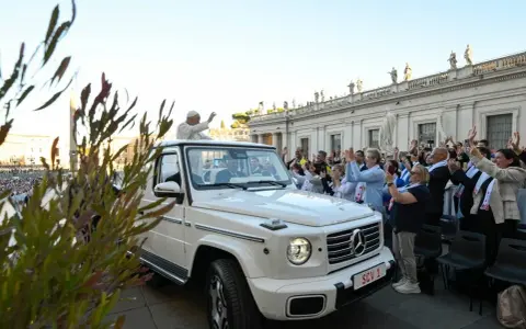 Papież Franciszek, mimo swojego vatican wiek, pozdrawia wiernych z białego mercedesa. Tłum wiwatuje, a niektórzy robią zdjęcia.